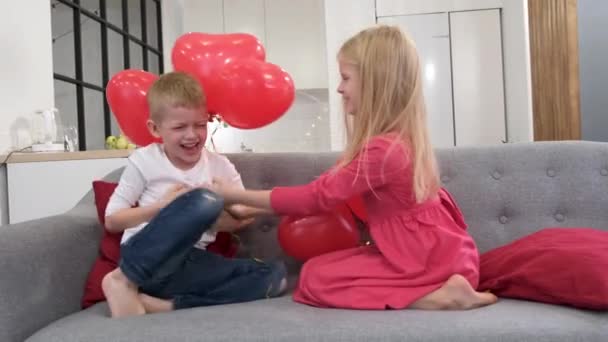 Kleine jongen en meisje spelen thuis met rode hartvormige ballonnen. We vieren Valentijnsdag. Langzame beweging. — Stockvideo