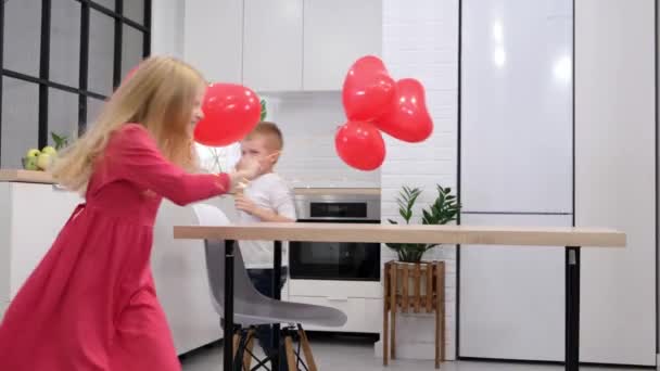 Dzieci biegające wokół stołu z czerwonymi balonami w kształcie serca w domu. Świętujemy Walentynki. Zwolniony ruch. — Wideo stockowe