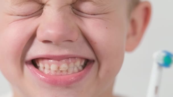 Ungar ler på nära håll. Porträtt leende pojke med elektrisk tandborste. Pojke gör roligt ansikte medan borsta tänderna på vit bakgrund. Hälsovård, tandhygien — Stockvideo