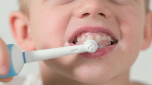 पांढर्या वीट पार्श्वभूमीवर इलेक्ट्रिक टूथब्रशसह दात घासणारा आनंदी स्मित मुलाचा मुलगा पोर्ट्रेट. आरोग्य सेवा, दंत स्वच्छता — स्टॉक व्हिडिओ