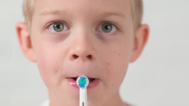 Fechar Retrato engraçado cara garoto com escova de dentes elétrica. menino escovar os dentes no fundo de tijolo branco. Saúde, higiene dentária — Vídeo de Stock