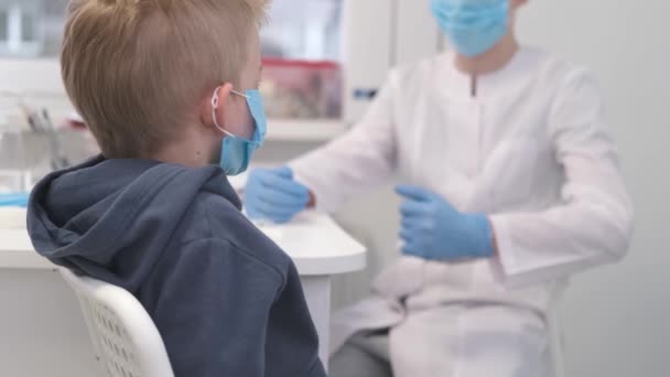 4k Rodinný lékař v ochranné masce mluvit s mladým chlapcem pacienta a mluvit během konzultace na zdravotní klinice. Lékař v laboratorní nemocnici. — Stock video