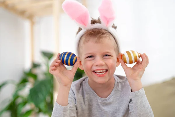 Buona Pasqua, ragazzi. Ragazzo in coniglio orecchie di coniglio in testa con uova colorate a casa. Allegro pazzo bambino sorridente. — Foto Stock