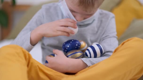 Paasjacht. Jongen in konijn konijnenoren op het hoofd en beschermende masker het verzamelen van kleurrijke eieren plezier hebben op bed thuis. — Stockvideo