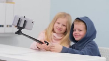 Çocuk blogcular takipçilerle konuşuyor, canlı yayında evde akıllı telefon ekranı arıyorlar. Küçük kız ve oğlan selfie çekiyorlar..