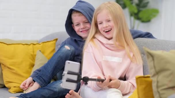 Kinderen bloggers praten met volgers, live streaming op zoek naar smartphone scherm thuis. Kleine jongen en meisje maken selfie. — Stockvideo