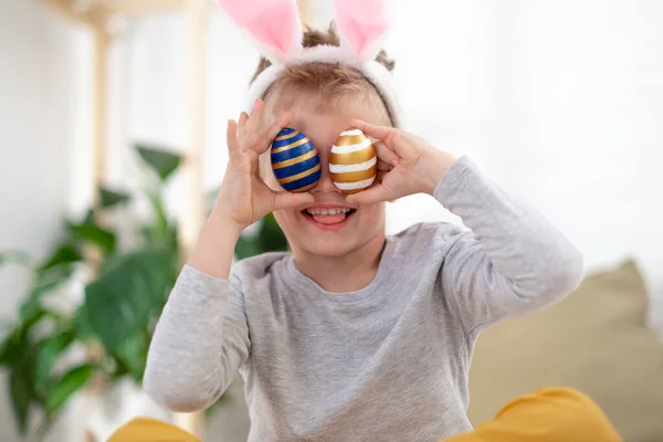 Frohe Osterkinder. Junge in Hasenohren auf dem Kopf mit bunten Eiern zu Hause. Fröhlich verrücktes lächelndes Kind. — Stockfoto
