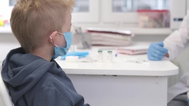 4k Семейный врач в защитной маске беседует с малышом пациентом и выступает во время консультации в поликлинике. Врач в лабораторной больнице. — стоковое видео