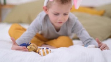 Paskalya avı. Tavşan kulaklı çocuk evde yatakta eğlenen renkli yumurtalar topluyor.. 