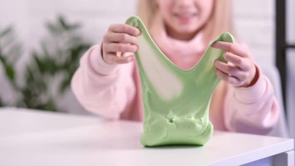 Gadis peregangan lendir hijau ke samping. tangan anak-anak bermain mainan lendir. Membuat lendir pada putih. Mainan cair Trendy menempel pada tangan dan jari. Rekaman 4k — Stok Video