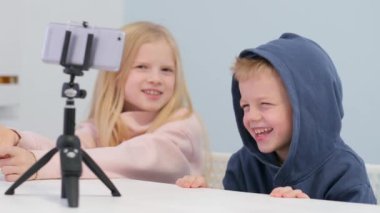 Çocuk blogcular takipçilerle konuşuyor, canlı yayında evde akıllı telefon ekranı arıyorlar. Küçük kız ve oğlan selfie çekiyorlar..