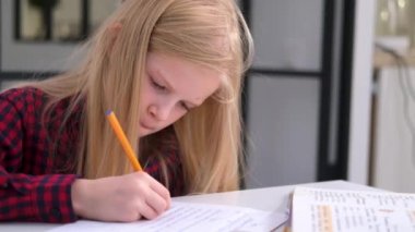 4k Sarışın liseli kız evde ders çalışıyor. Ödev yapıyor. Eğitim kitapları ve defterler masanın üstünde. Uzaklık öğrenimi çevrimiçi eğitim.