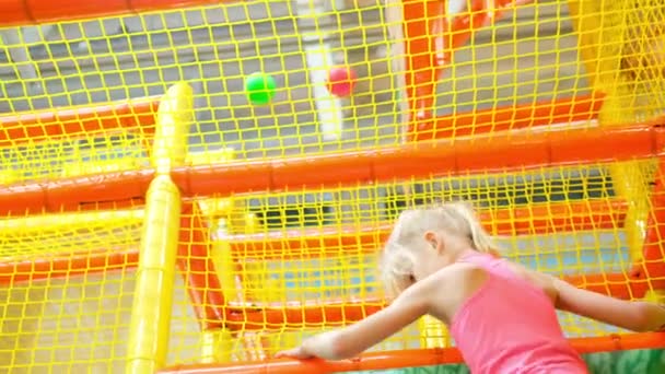 Spaß im Spielzimmer. Blondes Mädchen beim Spielen auf dem Indoor-Spielplatz, das aus bunten Plastikbällen im großen Trockenplanschbecken im Spielzentrum emporklettert. Freizeitbeschäftigung — Stockvideo