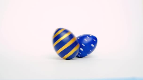 Los huevos de Pascua están rodando, golpeándose unos a otros en la mesa blanca. Huevos de moda de color clásico azul, blanco y dorado. Feliz Pascua. Estilo mínimo . — Vídeo de stock