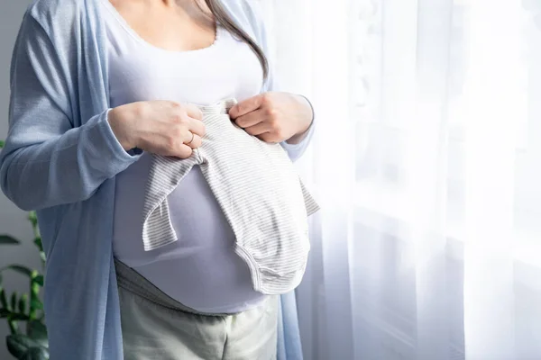 Cerrar las manos en la madre embarazada sosteniendo la ropa del bebé. Amante mujer esperando niño. Preparación para el parto, Chica gran vientre embarazo avanzado. — Foto de Stock