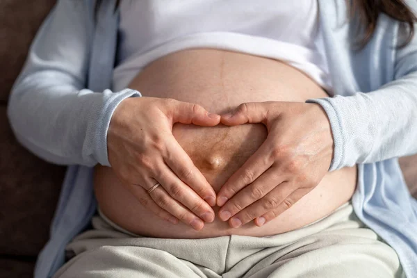 Мати кохання. вагітна жінка з великим животом передова вагітність відпочиває на дивані вдома роблячи серце руки — стокове фото