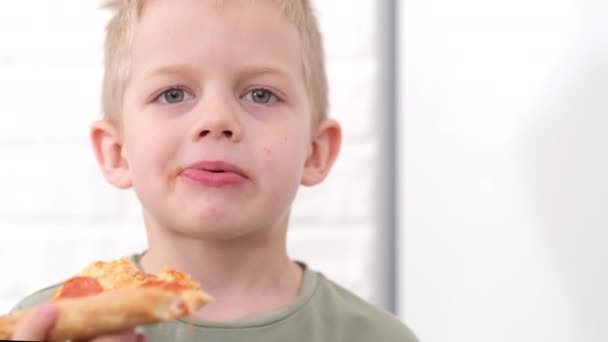 Портрет блондинка мальчик ест сыр Пицца улыбаясь близко. Счастливый ребенок жевания пиццы ломтик в помещении. Нездоровое фаст-фуд — стоковое видео