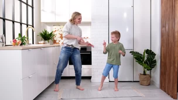 Eccitato mamma o babysitter e bambino ragazzo saltare ballare ridendo nella moderna cucina scandinava casa Felice famiglia madre e figlio divertirsi a giocare a cantare insieme a casa — Video Stock