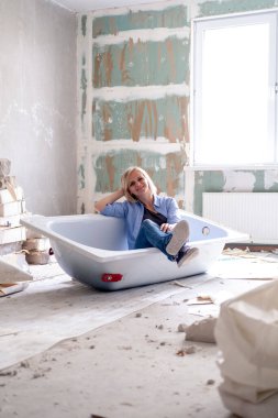 Yenileme dairesi. Yaratıcı hikaye genç mutlu kadın odanın ortasında küvette oturuyor. Boş duvarlar, kendi elleriyle tamir ettikleri ev.