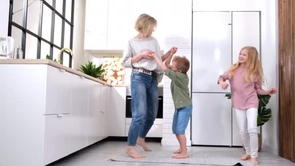興奮したお母さんやベビーシッターと2人の子供の男の子と女の子は、現代のスカンジナビアの家のキッチンで笑って踊るジャンプ幸せな家族の母親の娘の息子は、自宅で一緒に歌うことを楽しんで — ストック動画