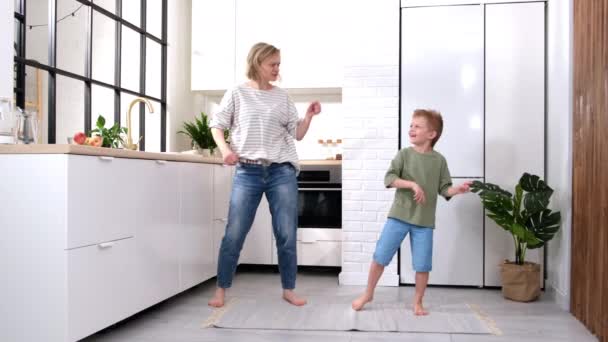 Eccitato mamma o babysitter e bambino ragazzo saltare ballare ridendo nella moderna cucina scandinava casa Felice famiglia madre e figlio divertirsi a giocare a cantare insieme a casa — Video Stock