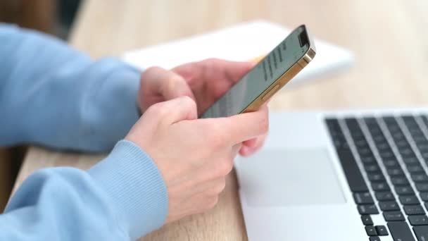 4k. férfi használ iPhone 12 okostelefon nyomja ujját, olvassa a közösségi média gépelés szöveget, vagy online vásárlás. Mobiltelefon két kézben otthon vagy a munkahelyen. laptop az asztalon 24.04.21 Szentpétervár Oroszország — Stock videók