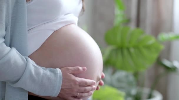 4k Madre incinta che tiene i vestiti del bambino in mano. Buona madre in attesa di un figlio. Preparazione per il parto, Ragazza grande pancia gravidanza avanzata. — Video Stock