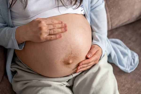 Вагітна жінка з великим черевом розвинена вагітність, що сидить на дивані вдома. Здорова вагітність та щаслива вагітність — стокове фото
