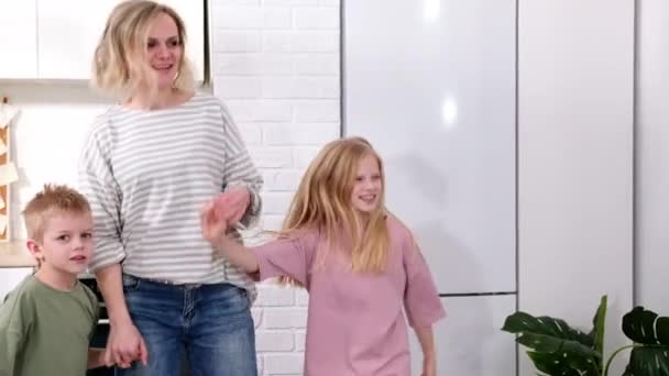 Emocionado mamá o niñera y dos niños niño y niña saltando bailando riendo en la cocina moderna casa escandinava feliz familia madre hija hijo divertirse disfrutar jugando cantando juntos en casa — Vídeos de Stock