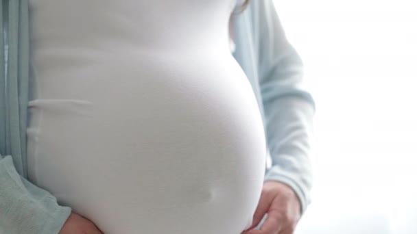 4k Zwangere aanstaande moeder tilt een t-shirt strelen haar buik. Vrouw handen die haar buik aanraken, wachtend kind. Voorbereiding voor de bevalling, Meisje grote buik gevorderde zwangerschap. — Stockvideo