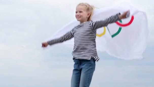 4k. Chica rubia ondeando bandera de los Juegos Olímpicos al aire libre sobre el cielo nublado puesta de sol. Niños fanáticos de los deportes. Juegos olímpicos de verano. 23.03.2020 San Petersburgo Rusia. — Vídeo de stock