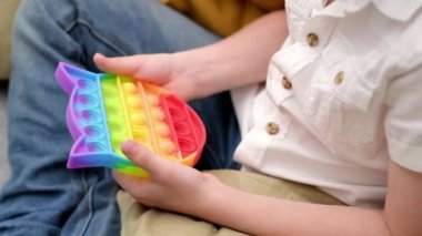 Çocuk oyuncağıyla oynuyor. Oğlan renkli gökkuşağı yumuşak silikon kabarcıklarına basıyor. Stres ve endişe giderici. Stresli çocuklar ve yetişkinler için hareketli moda oyunu.