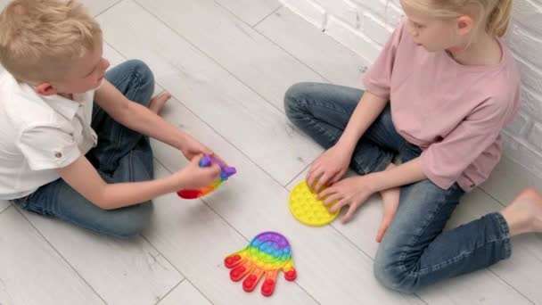 Crianças brincando com pop-lo brinquedo sensorial. menino e menina pressionando colorido arco-íris squishy bolhas de silicone macio. Alívio de estresse e ansiedade. Jogo de agitação na moda. Vista superior. — Vídeo de Stock