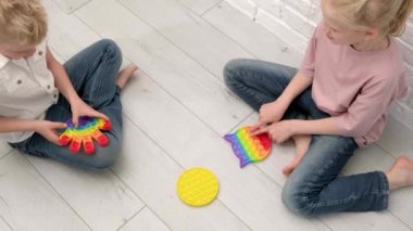 Çocuklar duyusal oyuncakla oynuyorlar. Oğlan ve kız renkli gökkuşağı yumuşak silikon kabarcıklarına bastırıyor. Stres ve endişe giderici. Kıpır kıpır bir oyun. Üst görünüm.