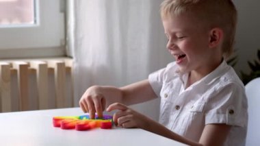 Çocuk oyuncağıyla oynuyor. Oğlan renkli gökkuşağı yumuşak silikon kabarcıklarına basıyor. Stres ve endişe giderici. Stresli çocuklar ve yetişkinler için hareketli moda oyunu.