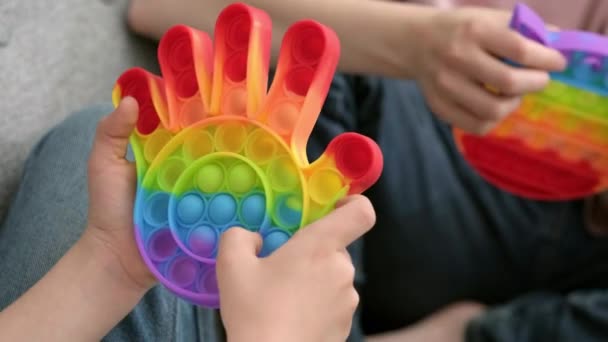 Crianças brincando com pop-lo brinquedo sensorial. menino e menina pressionando colorido arco-íris squishy bolhas de silicone macio. Alívio de estresse e ansiedade. Jogo de agitação na moda. — Vídeo de Stock