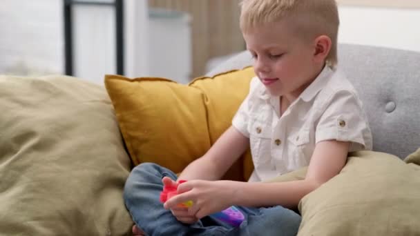 Kinder spielen mit Pop it sensorischem Spielzeug. Junge drückt auf bunte regenbogenfarbene quadratische weiche Silikonblasen. Stress- und Angstabbau. Trendiges Zappelspiel für gestresste Kinder und Erwachsene. — Stockvideo