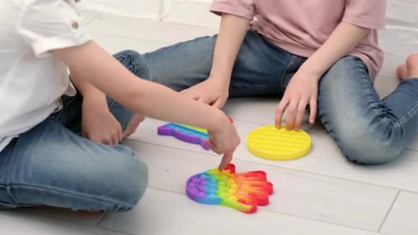 Crianças brincando com pop-lo brinquedo sensorial. menino e menina pressionando colorido arco-íris squishy bolhas de silicone macio. Alívio de estresse e ansiedade. Jogo de agitação na moda. Vista superior. — Vídeo de Stock