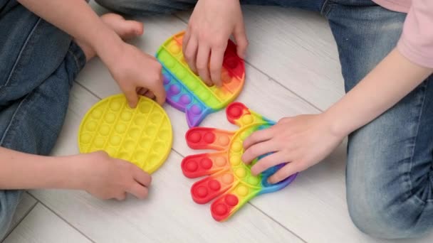 Los niños jugando con pop it juguete sensorial. niño y niña presionando sobre el arco iris colorido burbujas de silicona suave y blanda. Alivio de estrés y ansiedad. Juego de moda inquieto. Vista superior. — Vídeo de stock