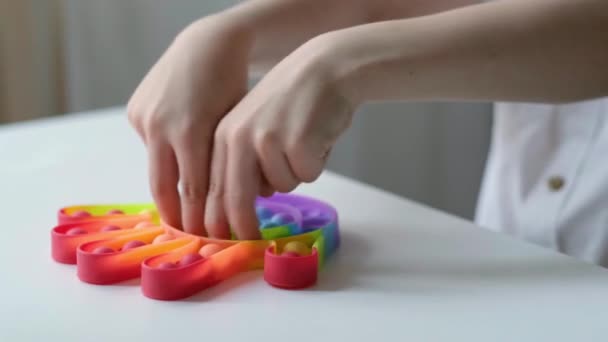 Kinder spielen mit Pop it sensorischem Spielzeug. Junge drückt auf bunte regenbogenfarbene quadratische weiche Silikonblasen. Stress- und Angstabbau. Trendiges Zappelspiel für gestresste Kinder und Erwachsene. — Stockvideo