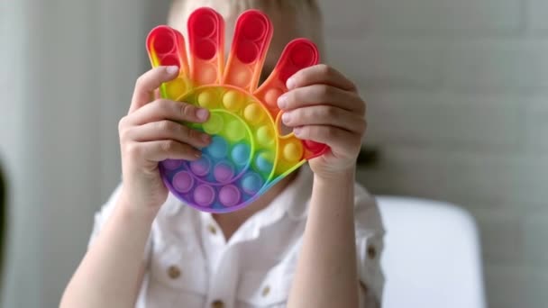 Child play with pop it sensory toy. Boy presses on colorful rainbow squishy soft silicone bubbles. Stress and anxiety relief. Trendy fidgeting game for stressed children and adults. — Stock Video