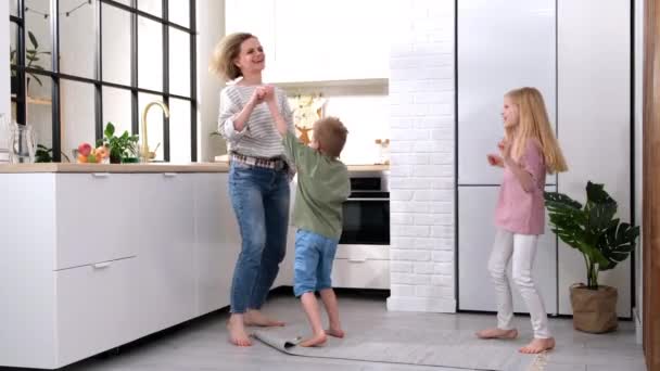 Emocionado mamá o niñera y dos niños niño y niña saltando bailando riendo en la cocina moderna casa escandinava feliz familia madre hija hijo divertirse disfrutar jugando cantando juntos en casa — Vídeos de Stock