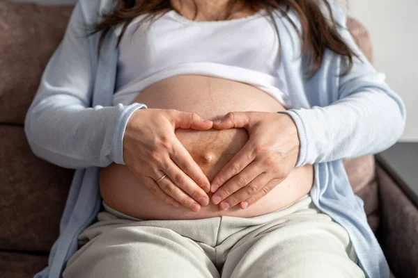 Мати кохання. вагітна жінка з великим животом передова вагітність відпочиває на дивані вдома роблячи серце руки — стокове фото