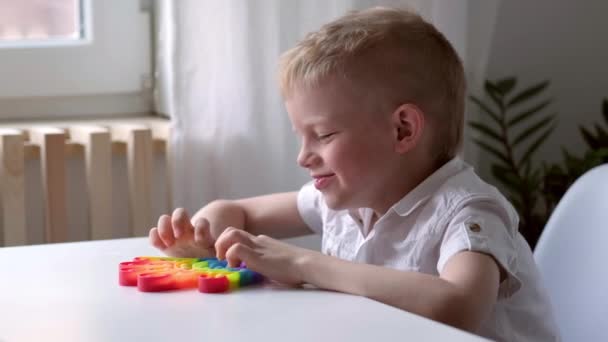 Lapsi leikkii pop se aistillinen lelu. Poika painaa värikkäitä sateenkaaren pehmeitä silikonikuplia. Stressi ja ahdistuneisuus. Trendikäs fidgeting peli stressaantunut lapsille ja aikuisille. — kuvapankkivideo