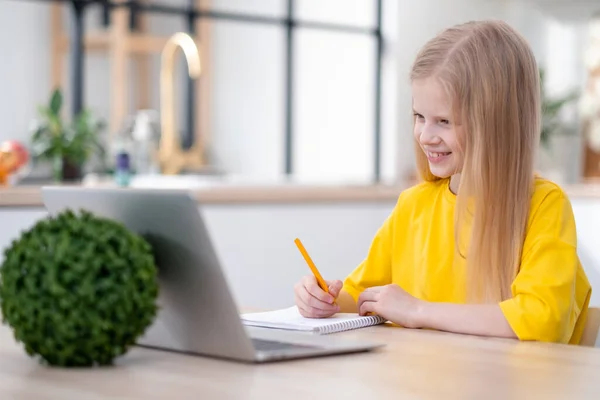 Blondynka ucząca się w domu odrabiająca lekcje z laptopem. Kształcenie online na odległość. Wracamy do szkoły. — Zdjęcie stockowe