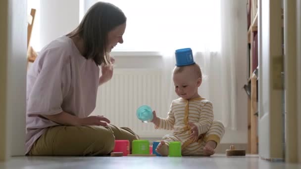 Kleine baby meisje en mama spelen thuis met kleurrijk speelgoed zittend op de vloer. Moeder en dochter lachen samen plezier — Stockvideo