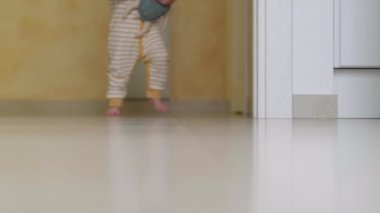 Bebek ilk adımı atıyor. Evdeki beyaz zeminde yürüyen tanınmayan küçük kız çocuğu. Mutfakta yalınayak bacaklar..
