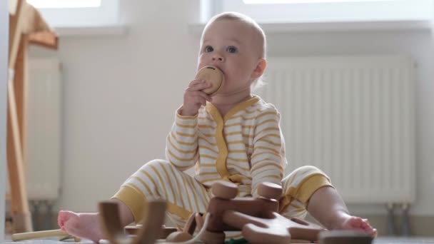 Eco juguete de madera juego de bebé. Pequeño niño caucásico inteligente jugando juguetes naturales en el suelo en casa. Juegos educativos para el desarrollo temprano. Pequeño niño pone juguete en su boca — Vídeo de stock