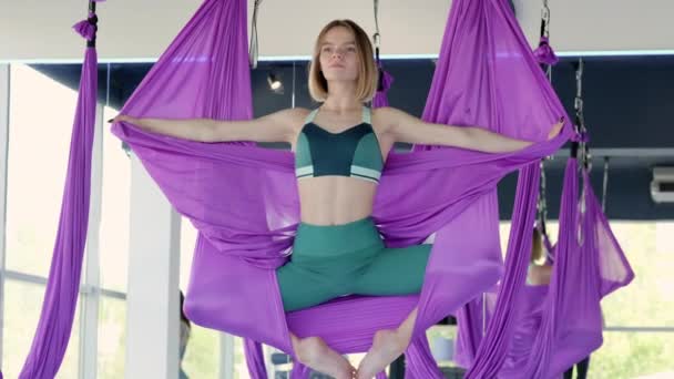 空中ストレッチスイングでポートレート若い笑顔の女性の練習.フィットネスクラブでの紫ハンモックでの空中飛行ヨガの練習 — ストック動画