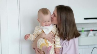 Küçük çocuk gülüyor, eğleniyor ve kameraya bakıyor. Mutlu Neşeli Aile. Anne ve Bebek Öpüşmesi.